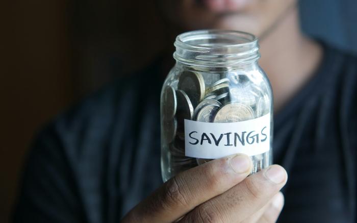 a man holding a jar with a savings label on it by Towfiqu barbhuiya courtesy of Unsplash.